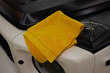 A yellow towel lies on a car hood near an automotive