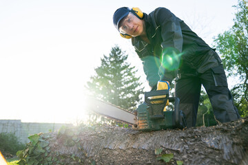 Wall Mural - A man in uniform cuts an old tree in the yard with an electric saw.