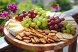 Cheese, crackers and grapes served on a round wooden platter outside on the porch in the sun 