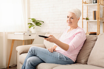 Wall Mural - Senior Woman Sitting on Couch Holding Remote Control