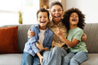 © Maria Vitkovska - Happy mother and two kids sitting on the sofa in room at home, embracing, looking at camera