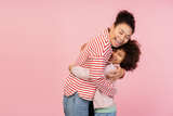 Fototapeta  - Happy young mother hugging her little daughter while standingin studio, isolated on pink background