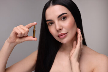 Canvas Print - Beautiful young woman holding skincare ampoule on grey background