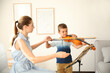 © New Africa - Young woman teaching little boy to play violin indoors
