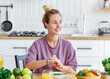 Young beautiful smiling woman eating fresh organic vegetarian salad sitting in the kitchen at home