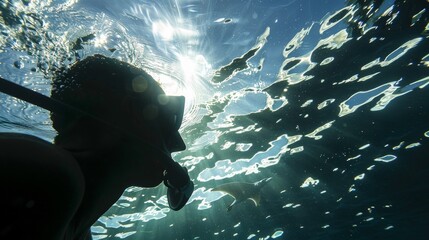 Wall Mural - An underwater perspective of a snorkeler amidst sunbeams piercing through the ocean surface