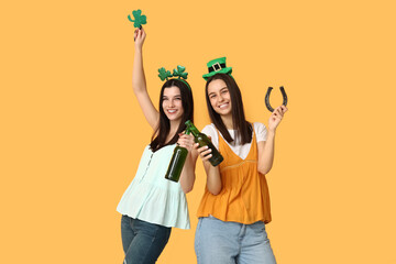 Poster - Beautiful young women with bottles of beer, clover and horseshoe on yellow background. St. Patrick's Day celebration