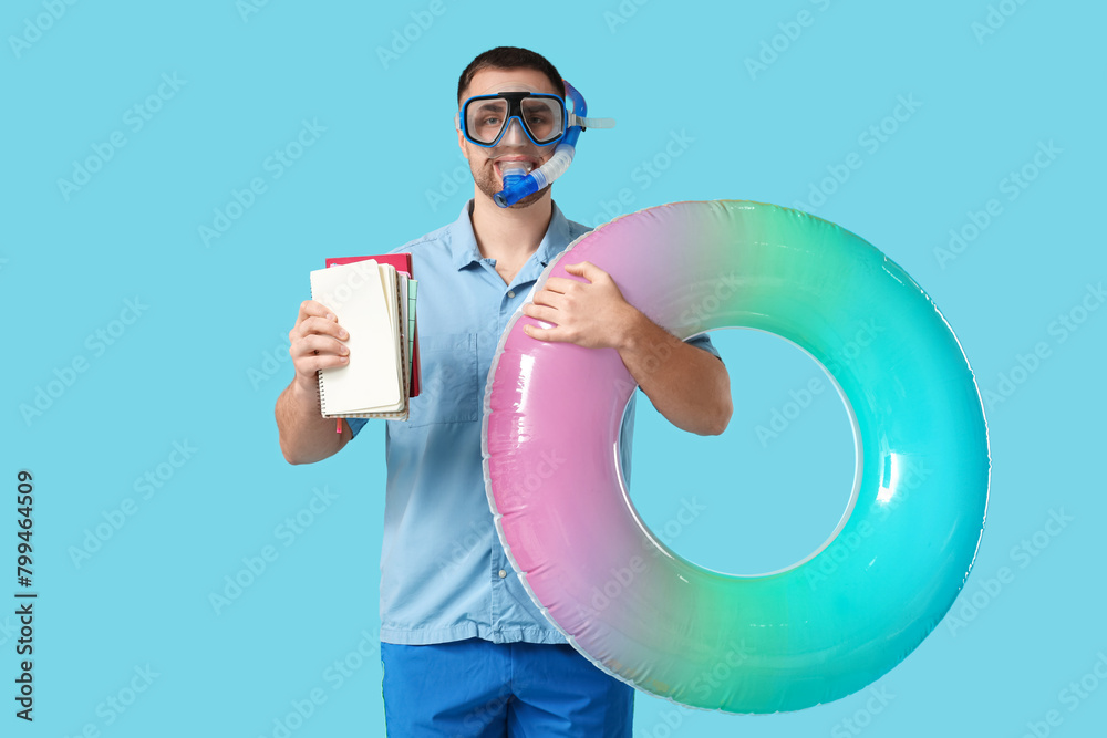 Happy office worker in diving mask with snorkel holding inflatable ring and notebooks on blue background