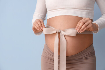 Wall Mural - Young pregnant woman with bow on her belly against blue background, closeup