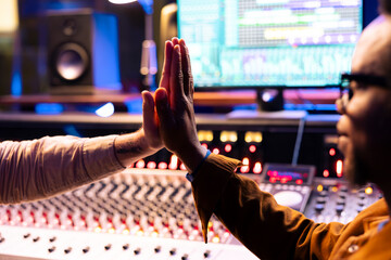 Fototapete - Pleased artist doing high five gesture with sound designer after finishing a song, processing and editing music for his new album. Singer and producer celebrating successful tracks in studio.