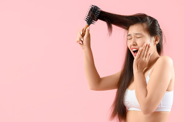 Sticker - Beautiful young shocked Asian woman brushing her hair on pink background