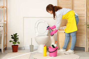 Canvas Print - Young woman cleaning toilet bowl in light bathroom