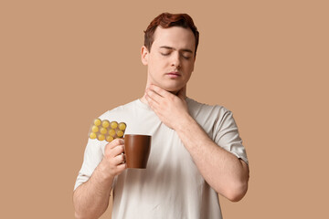 Poster - Young man with sore throat, hot tea and pills on beige background