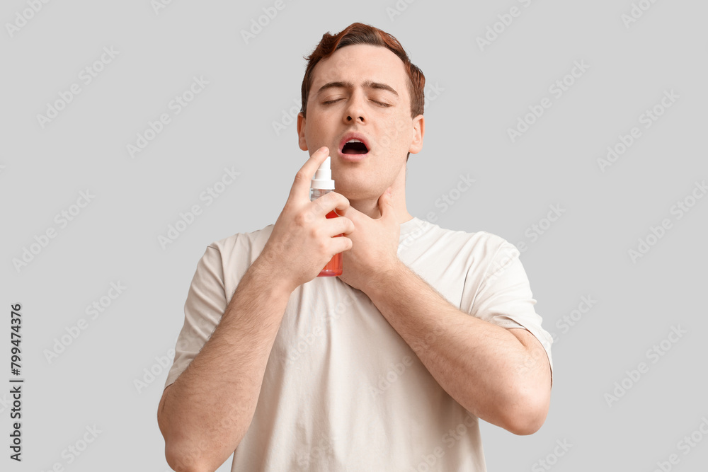 Young man with sore throat and spray on light background