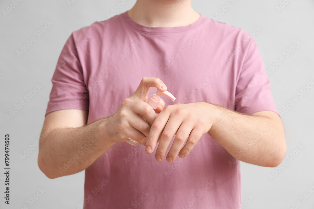 Young man with sanitizer on light background, closeup