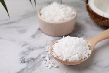 Coconut flakes in wooden spoon on white marble table, closeup. Space for text