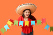 Happy young woman in Mexican sombrero hat and with garland on orange background