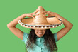 Beautiful young African-American woman in sombrero hat on green background