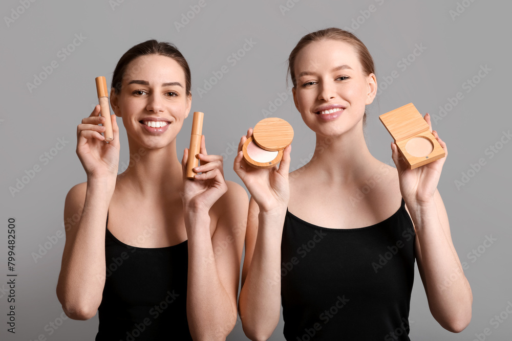 Beautiful young sisters with makeup products on grey background