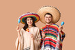 Beautiful young happy couple in sombrero hats with maracas on beige background. Cinco de Mayo celebration