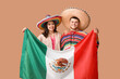 Beautiful young happy couple in sombrero hats with Mexican flag on beige background. Cinco de Mayo celebration