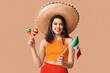 Beautiful young happy woman in sombrero with Mexican flag and maracas on beige background. Cinco de Mayo celebration