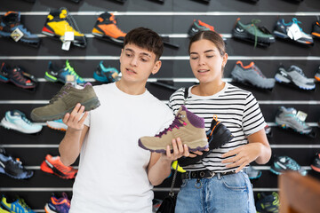 Wall Mural - Guy with girlfriend, view specialized shoes in store, near showcase with summer trecking cross-shoes, buyers talk about advantages and disadvantages of hiking shoes