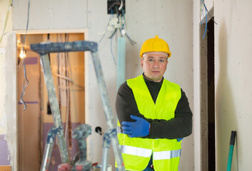 Wall Mural - Caucasian repair man standing in apartment at stepladder and looking at camera.