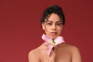 Poster - Beautiful young African-American woman with pink lily flower on red background