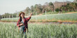 © Satori Studio - Female farmer with a digital tablet points towards the horizon while standing in a vibrant green wheat field.