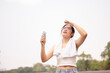 A woman holds a small fan and wipes her sweat on her face while walking outdoors on a hot day.