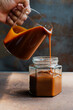 Homemade caramel sauce pouring on a glass jar on rustic table