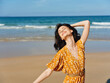 Woman in a yellow dress standing on the beach with arms outstretched in a peaceful and serene moment