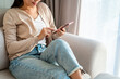 Young Asian woman relaxing and using mobile phone on a sofa at home in the morning