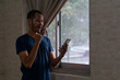 Excited young Asian man standing beside of window with smart phone