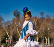 a little girl dancing flamenco dressed in a white dress with ruffles and blue fringes in a famous square in seville, spain. The girl has flowers on her head. Flamenco, cultural heritage of humanity.