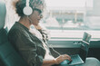 Young woman work on laptop with headset sitting on bus seat. Travel business lifestyle female people. Modern lady smiling and enjoying trip as passenger on transport public vehicle. Technology online