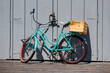 Colorful old bike with mint frame and red rims leaning locked on grey wooden door in bright sunshine. Wooden box on the luggage rack. Idyllic still life scene on a pier in California.