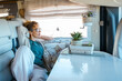 One woman relaxes inside a camper van motorhome rv vehicle. lady loves to relax sitting on the sofa looking outside. Freedom travel concept. Spring weekend traveler female lifestyle. Independence