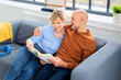 Blond haired woman reading a book and mid aged man sitting next to her on the sofa at home