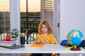 Fototapete - Portrait of cute child school boy writing school homework at table in room. School and education kids concept. Clever kid with school supplies doing homework at home.