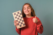 A girl is holding a chess board and smiling. She is giving a thumbs up. Concept of happiness and excitement about playing chess