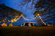 camping tent on grass courtyard and warm night light under dark blue sky. Family vacation picnic on holiday relax.