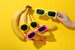 Bananas, sunglasses and hand on yellow background, top view