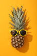 Sunglasses on pineapple on orange background, top view