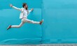 Stylish man jumping in the air in front of blue wall
