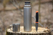 thermos, mug and knife on a wooden stump in the forest