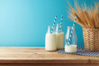 Jewish holiday Shavuot concept with milk bottles and wheat ears in basket on wooden table over blue background