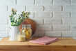 Empty wooden l table with tablecloth, plant, food jars and cutting board over white brick wall  background.  Kitchen mock up for design and product display.