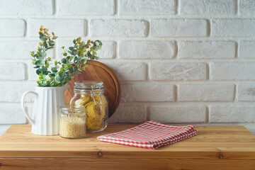 Wall Mural - Empty wooden l table with tablecloth, plant, food jars and cutting board over white brick wall  background.  Kitchen mock up for design and product display.